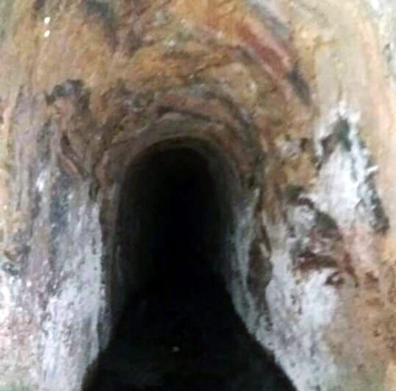 Interior de galeria de mina escavada na rocha, estreita e escura, com o túnel se afunilando ao fundo.