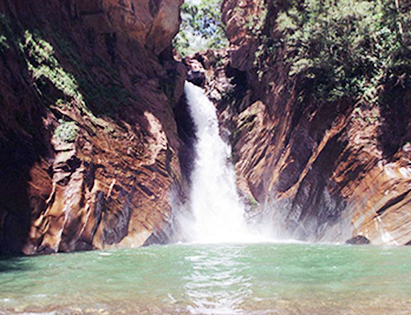 Poço de águas claras ao pé de uma cachoeira, cercado por rochas e vegetação.