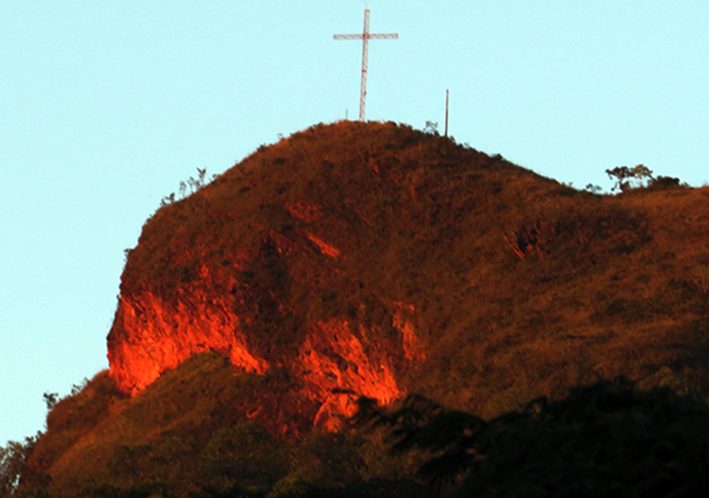 O Morro da Santa Cruz, com a rocha avermelhada exposta no cume e a cruz de metal no alto.